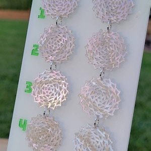 May include: A pair of dangle earrings with four white, iridescent, circular, openwork charms on each earring. The charms are attached to each other with silver jump rings.