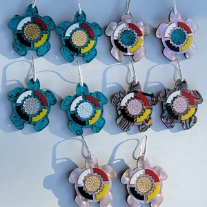 May include: A set of 9 pairs of turtle earrings. The earrings are made of turquoise, abalone, and mother-of-pearl. Each turtle has a colourful circle design in the centre.