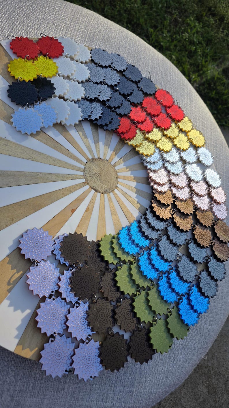 Puede incluir: Una colecci&oacute;n de colgantes coloridos en forma de estrella dispuestos en arco. Los colgantes son de varios colores, incluyendo rojo, amarillo, negro, azul y verde. Se exhiben sobre una superficie de madera con un dise&ntilde;o de rayos de sol.