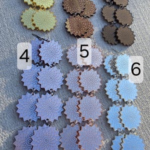 Puede incluir: Colecci&oacute;n de seis pares de pendientes con un dise&ntilde;o floral &uacute;nico. Los pendientes est&aacute;n disponibles en oro, marr&oacute;n y tonos de azul y morado. Fabricados con un material reflectante.