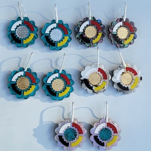 May include: A set of six pairs of earrings featuring a colourful, circular design with a gold centre. The earrings are made of various materials, including turquoise, white, black, red, and yellow.