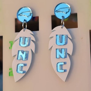 May include: A pair of white feather earrings with blue UNC lettering and a blue North Carolina state outline charm.