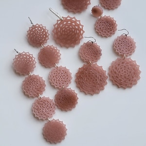 May include: A set of pink, intricate, circular earrings with a delicate, lacy design. The earrings are available in various sizes and styles, including single, double, and triple drop designs.