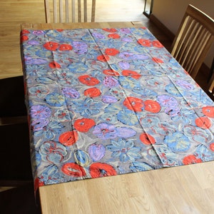 Könnte beinhalten: Ein rechteckiges Tischtuch mit einem Blumenmuster in Rot-, Blau- und Lilatönen auf grauem Hintergrund. Das Tischtuch liegt auf einem Holztisch, umgeben von Holzstühlen. Das Blumenmuster ist das Hauptmerkmal.