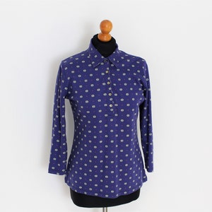 Pode incluir: Uma camisa azul de manga comprida com um padrão de bolinhas brancas. A camisa tem um colarinho abotoado e uma aba de botões.