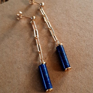 Op de afbeelding: Een paar gouden kettingoorbellen met blauwe lapis lazuli cilinder hangers.
