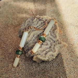 May include: A pair of dangle earrings with white shell and green stone beads. The earrings are on a white coral-like surface.