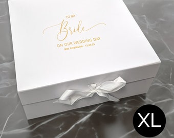 May include: A square white gift box with a white ribbon closure. The lid features gold foil text that reads TO MY Bride ON OUR WEDDING DAY MRS ROBINSON - 12.06.25. A black circular icon with the white text XL is positioned in the lower right corner.