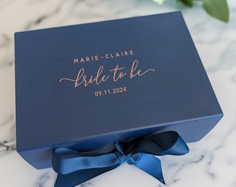 May include: A navy blue gift box with a satin ribbon tied around it. The box is personalized with the text "Marie-Claire bride to be 09.11.2024" in rose gold lettering.