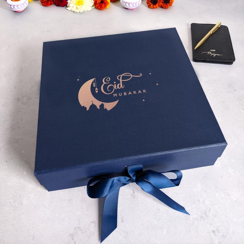 May include: A navy blue gift box with a gold foil crescent moon and the text "Eid Mubarak". The box is tied with a navy blue ribbon.