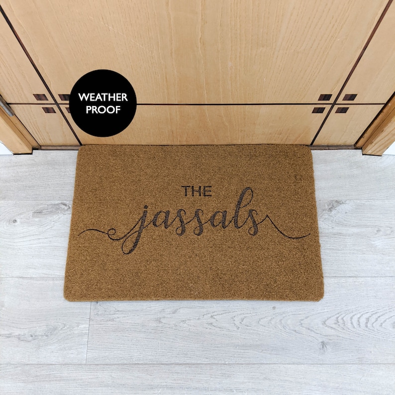May include: A brown coir doormat with the text "THE JASSALS" in black cursive lettering. The doormat is weatherproof.