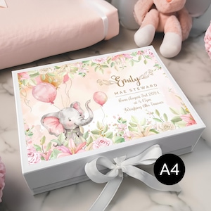 Peut inclure: Boîte à souvenirs blanche avec un motif floral et un éléphant rose tenant des ballons. La boîte est ornée d'un ruban blanc et le texte "Emily Mae Steward Née le 3 août 2024, à 16h47  Poids : 2,8 kg" imprimé sur le couvercle.
