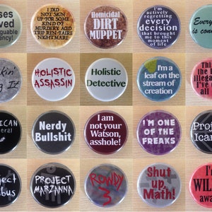 May include: A collection of 16 round buttons with various colourful designs and text. The buttons feature humorous and sarcastic phrases, including "Cases solved with arguable efficiency!" and "I'm one of the freaks".