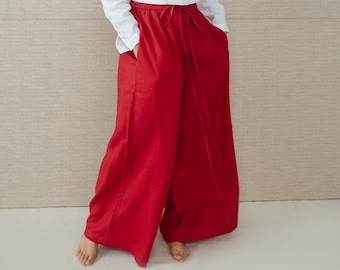 May include: A woman wearing a white linen shirt and red linen pants. The pants have a drawstring waist and wide legs.