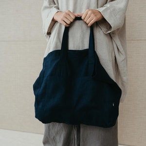 May include: A person is holding a dark blue tote bag with a single pocket on the front. The bag is made of a thick, textured fabric.