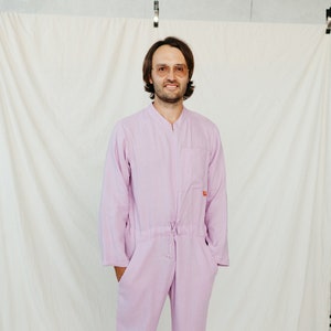May include: A person wearing a light purple jumpsuit with a zipper and a drawstring waist. The jumpsuit has a pocket on the left side.