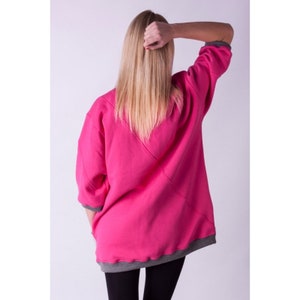 May include: A pink sweatshirt with a grey trim around the neckline and cuffs. The sweatshirt has a diagonal seam down the back.