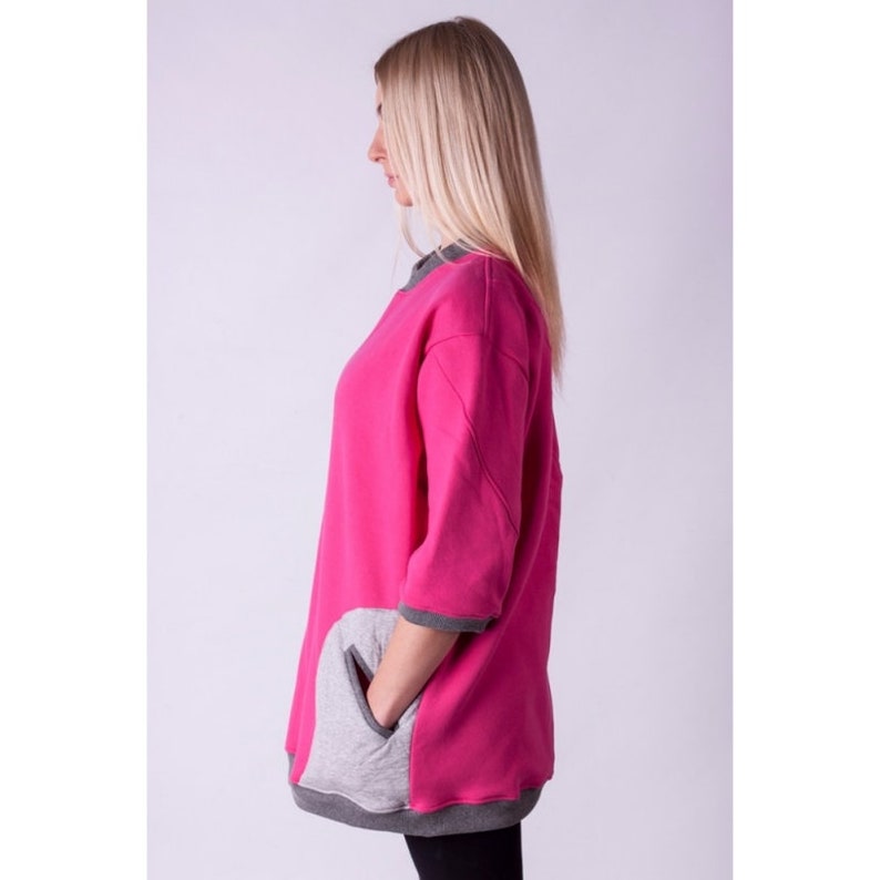 May include: A pink and gray oversized sweatshirt with a large pocket on the side. The sweatshirt has a relaxed fit and a round neckline.