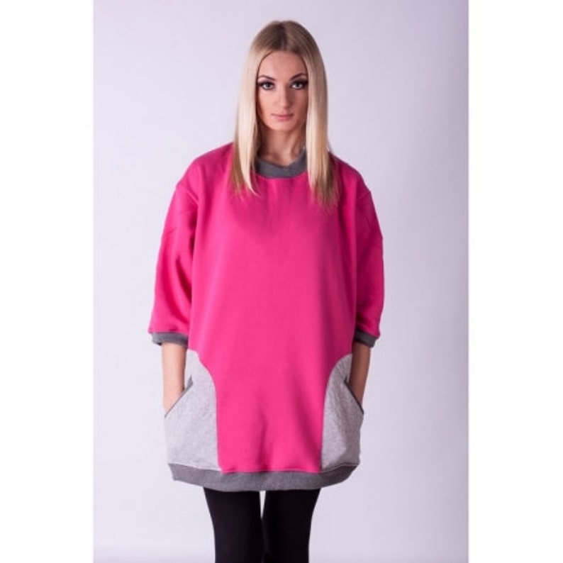 May include: A pink sweatshirt with grey accents on the pockets and sleeves. The sweatshirt has a relaxed fit and a round neckline.