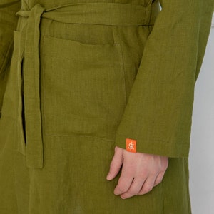 May include: A green linen robe with a belt and a pocket. The robe has a small orange label with the letters "SK" on the sleeve.