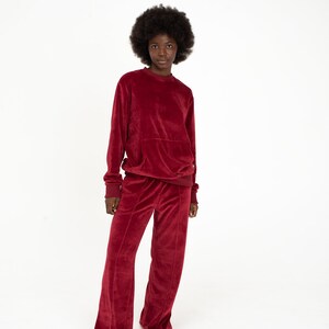 K&ouml;nnte beinhalten: Eine Frau tr&auml;gt ein rotes Samt-Sweatshirt und eine passende weite Hose. Das Outfit ist eine bequeme und stilvolle Wahl f&uuml;r Freizeitkleidung.
