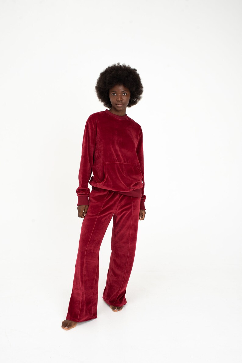K&ouml;nnte beinhalten: Eine Frau tr&auml;gt ein rotes Samt-Sweatshirt und eine passende weite Hose. Das Outfit ist eine bequeme und stilvolle Wahl f&uuml;r Freizeitkleidung.