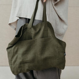 May include: A large, olive green linen tote bag with a single pocket on the front. The bag has thick, sturdy straps.