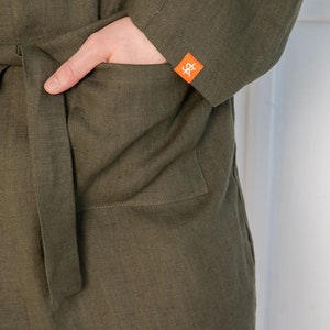 Op de afbeelding: Een groene linnen badjas met een opgestikte zak aan de linkerkant. De zak heeft een klein oranje label met de letters "S&" erop.