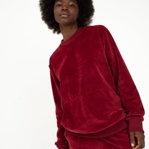 K&ouml;nnte beinhalten: Ein weinroter Samt-Sweatshirt mit einer K&auml;ngurutasche und einer passenden Hose. Der Pullover hat lange &Auml;rmel und einen Rundhalsausschnitt.