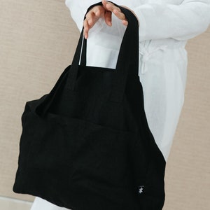 May include: A large black tote bag with a single pocket on the front. The bag has a small logo on the bottom right corner.