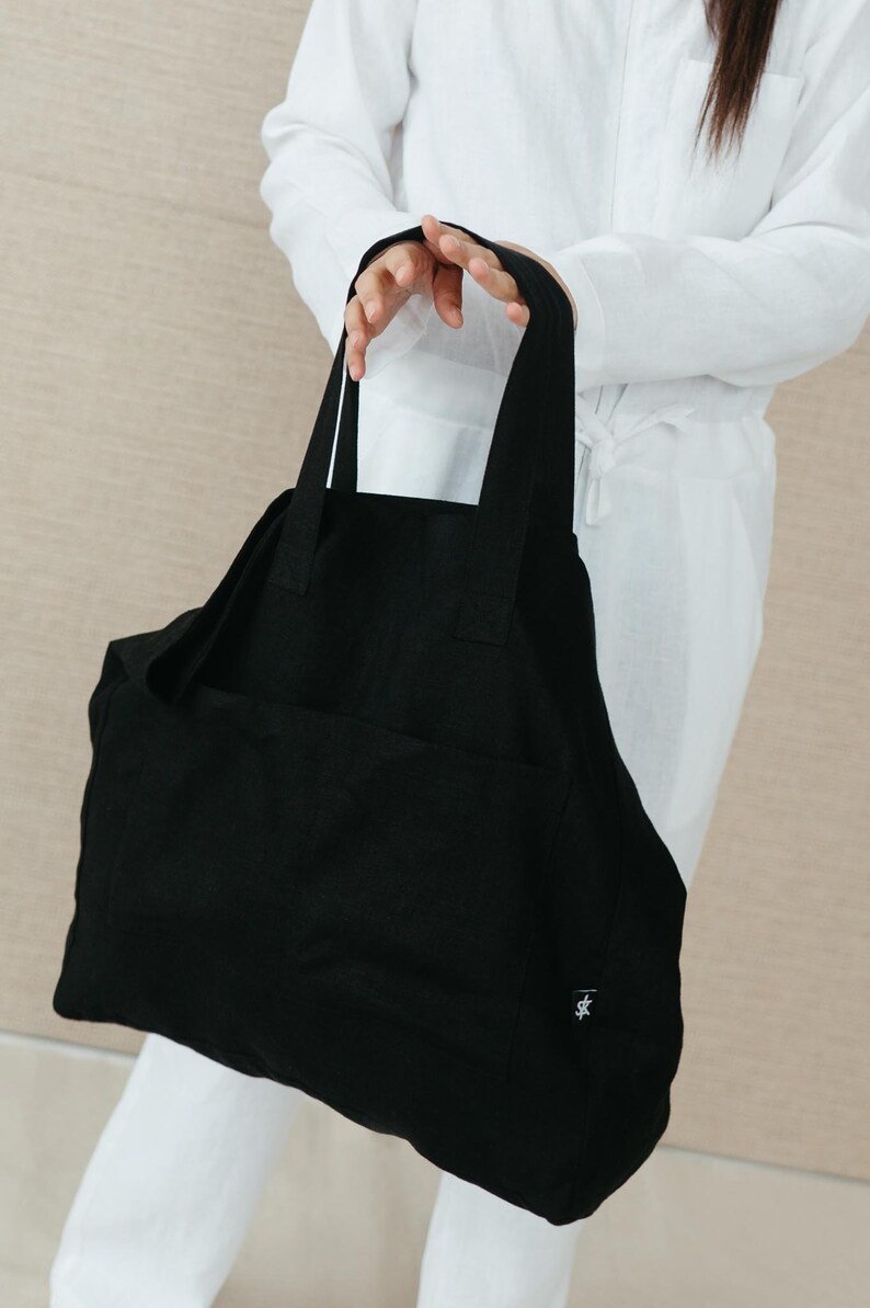 May include: A large black tote bag with a single pocket on the front. The bag has a small logo on the bottom right corner.