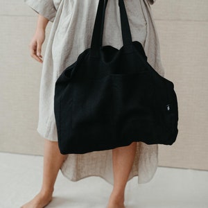 May include: A black canvas tote bag with a single pocket on the front. The bag has a simple design and is made of a durable material.