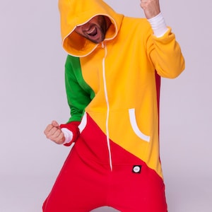 Op de afbeelding: Een persoon draagt een rood, geel en groen hooded jumpsuit met een witte rits. De persoon knielt met zijn armen omhoog.