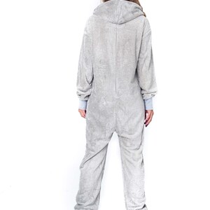 May include: A grey hooded onesie with long sleeves and a zip closure. The onesie is made of a soft, fuzzy material.