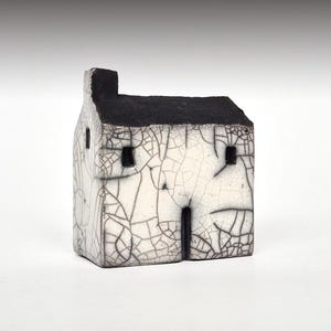 Könnte beinhalten: Ein kleines weißes Keramikhaus mit schwarzem Dach und Fenstern. Das Haus hat eine craquelée Glasur.