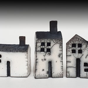 Op de afbeelding: Drie kleine witte keramische huisjes met zwarte daken en ramen. De huisjes zijn in een rij van links naar rechts geplaatst.