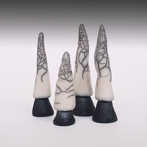 May include: Four ceramic sculptures with a cone-like shape. The sculptures are white with a black, web-like pattern and sit on black bases. The background is a gradient of white to light grey.