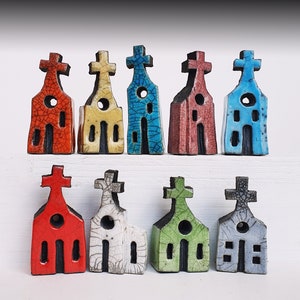 Może przedstawiać: Dziesięć miniaturowych ceramicznych budynków kościelnych w różnych kolorach, w tym czerwonym, niebieskim, zielonym, żółtym i białym. Każdy kościół ma krzyż na szczycie i okno z przodu.
