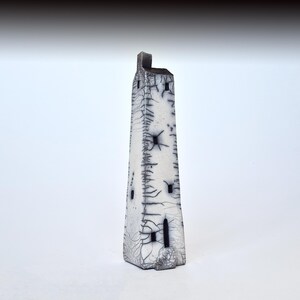 May include: A white ceramic tower with black details and a textured surface. The tower has several small windows and a pointed roof.