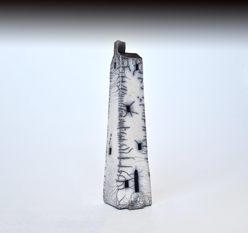 May include: A white ceramic tower with black details and a textured surface. The tower has several small windows and a pointed roof.