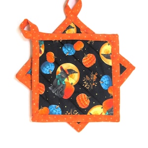 May include: Square quilted Halloween-themed pot holder with orange polka dot trim and hanging loop. The black fabric features pumpkins, a full moon, and a witch cat. The pot holder is approximately 8 inches square.