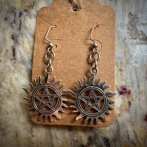 May include: A pair of silver earrings with a pentagram inside a sunburst design.