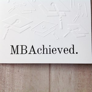 May include: White card with an embossed design of graduation caps and the text "MBA Achieved."
