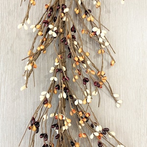 May include: A long, cascading garland of faux berries in shades of cream, burgundy, and orange. The garland is made of thin, brown twigs and is perfect for adding a touch of rustic charm to your home decor.
