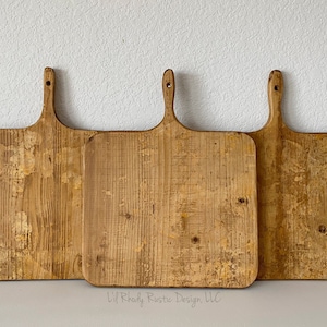 May include: Three rustic wooden cutting boards with handles. The boards are rectangular with rounded corners and a hole in the handle for hanging. The wood has a distressed, aged appearance with visible grain and knots.