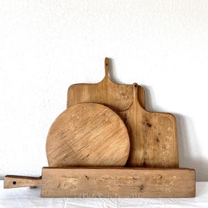 May include: A collection of four wooden serving boards with natural grain patterns. The set includes a long rectangular board, a circular board, and two rectangular boards with handles. The text Lil Rhody Rustic Design LLC is visible.