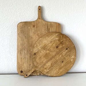 May include: Two wooden cutting boards, one rectangular and one round, with handles. The boards have a rustic, weathered appearance with visible wood grain and knots. The rectangular board is taller than the round one.