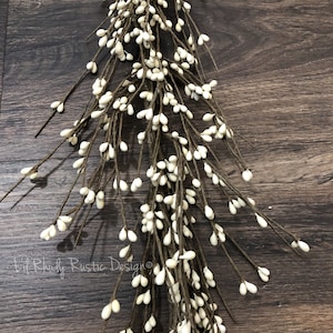 May include: A long white berry garland with brown stems. The garland is hanging on a wood background.
