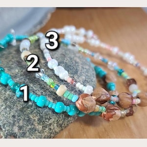 Könnte beinhalten: Drei Perlenarmbänder mit den Nummern 1, 2 und 3. Armband 1 besteht aus türkisfarbenen Perlen und braunen, strukturierten Perlen. Armband 2 enthält weiße, grüne und klare Perlen. Armband 3 besteht aus weißen, rosa und blauen Perlen mit braunen Akzenten.