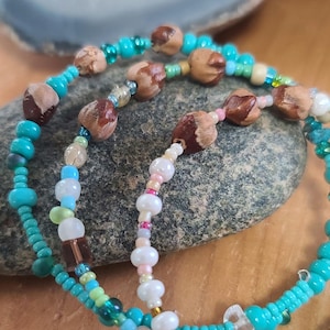 May include: A multi-strand beaded necklace with turquoise, green, and white beads. The necklace features wooden beads and a pearl-like bead.